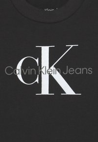 T-shirt en coton noir avec un grand logo "CK" blanc et le texte "Calvin Klein Jeans" dans une police simple et audacieuse. Design classique à col rond.