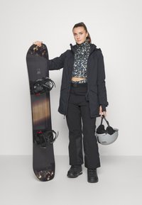 Vêtements d'extérieur noirs, haut à motifs et pantalons de neige. Tenant un snowboard avec fixations et un casque gris. Textures lisses et design fonctionnel.
