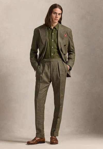 Prispôsobený šedý a zelený károvaný oblek s skladanými nohavicami, doplnený tmavozelenou košeľou a hnedými koženými topánkami. Súčasťou je vreckovka do saka.