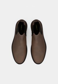 Chaussures en cuir marron à enfiler avec des panneaux élastiques sur les côtés et une semelle en caoutchouc noir texturé. Marque visible à l'intérieur des chaussures.