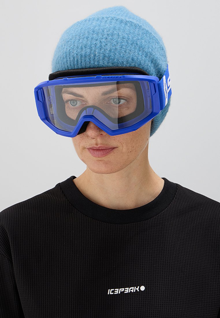 Skibrille mit einem blauen Rahmen und klaren Gläsern, getragen mit einer hellblauen Strickmütze und einem schwarzen, strukturierten Langarmshirt.
