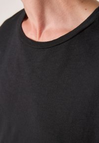 Črna majica s kratkimi rokavi, gladke teksture in okroglim ovratnikom. Tkanina je videti lahka s subtilnim sijajem.