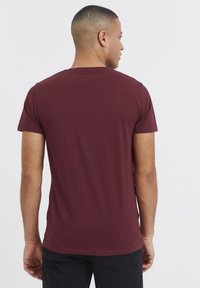 Burgundy bomulds t-shirt med korte ærmer, rund halsudskæring og en afslappet pasform. Glat tekstur og minimalistisk design uden mønstre.