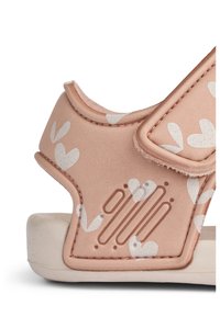 Απαλό ροζ σανδάλι με λευκά σχέδια καρδιάς, κατασκευασμένο από μαλακό υλικό, με λουράκι βέλκρο και υφασμάτινες λεπτομέρειες στην πλευρά.