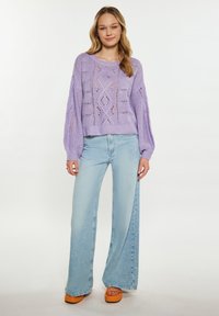 Hellviolettes, gestricktes Sweater mit Lochmuster, kombiniert mit hochgeschnittenen, hellblauen Schlagjeans und orangen Plateausandalen.