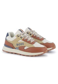Sapatos desportivos com um upper de tecido bege, detalhes em couro castanho e pormenores azuis. A sola é texturizada para oferecer aderência.