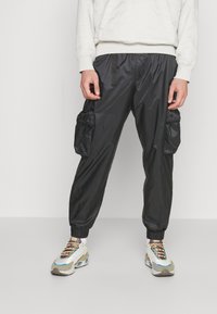 Black, lightweight cargo pants with elastic cuffs and side pockets, featuring a smooth, shiny texture and adjustable waist drawstring.
