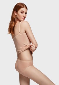 Lichtbeige topje met dunne bandjes, gecombineerd met bijpassende naadloze bikini slipjes. Glad textuur, figuurvolgende ontwerp, minimale details.