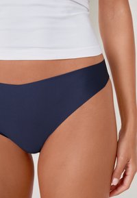 Navyfarbene Bikinihose mit glatter Textur, niedriger Schnitt und minimalistischen Design. Kombiniert mit einem weißen, enganliegenden Tanktop.