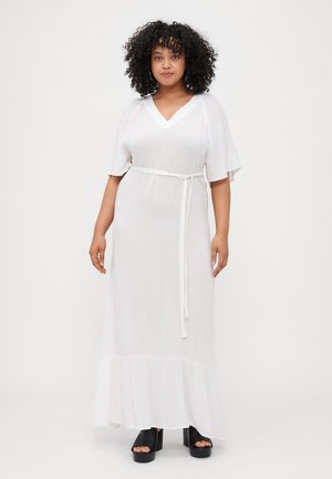 Abito maxi bianco con maniche corte e scollatura a V. Presenta una cintura annodata in vita e un orlo volante. Indossato con scarpe con plateau nere.