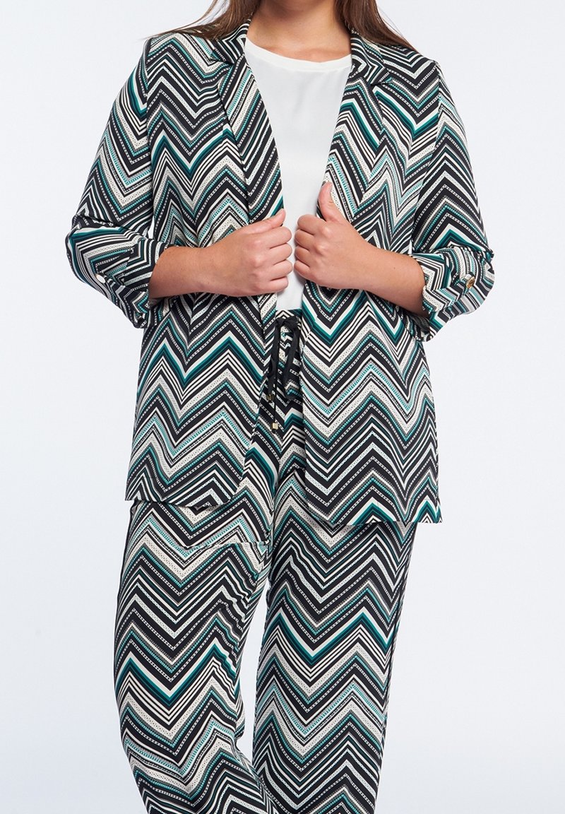 Ensemble blazer et pantalon à motif chevron noir et blanc avec des accents bleu sarcelle ; possède une coupe décontractée et des manches retroussées, confectionné dans un tissu lisse.