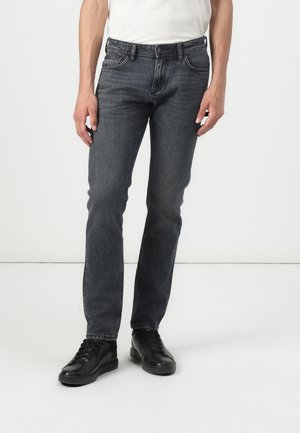 Mørkeblå jeans laget av denim, med rette ben, fem lommer, frontlukking med knapp og subtil blekning. Kombinert med svarte sko.