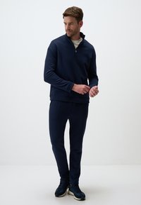 Granatowy sweter z kołnierzem na zamek błyskawiczny do połowy, w zestawie z dopasowanymi spodniami. Materiał jest gładki, z luźnym krojem i bez wyraźnych wzorów.
