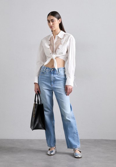 Vit kortärmad topp med spetsdetaljer, knuten i midjan, ihop med ljusblå vida jeans. Svart handväska och silvriga ballerinas fulländar outfiten.