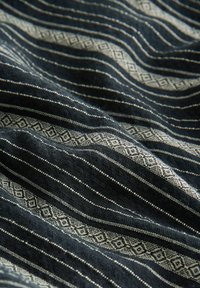 Gewebter Stoff mit dunkelblauen und cremeweißen Streifen sowie geometrischen Mustern, der eine strukturierte Oberfläche und einen subtilen Glanz aufweist.