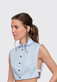 Light blue cropped shirt with short sleeves, button front, and a collar; features a left chest pocket and contrasting black buttons.