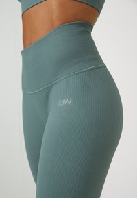 Colanți teal cu talie înaltă, fabricați dintr-un material ribbed, având o textură netedă și un mic logo pe coapsă.