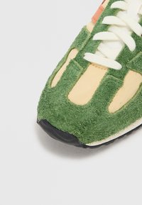 Adidași verzi și galbeni cu un finisaj texturat, păros, având șireturi albe și o talpă din cauciuc negru. Designul include secțiuni decupate.
