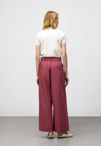 Wijdvallende broek in een diepe rozenkleur, gemaakt van een lichtgewicht stof, met een elastische tailleband en twee achterzakken. Effen witte top met korte mouwen.