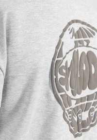 Camiseta de algodón gris con un gran logo texturizado en un tono más oscuro. El diseño incluye un contorno del globo y texto estilizado.