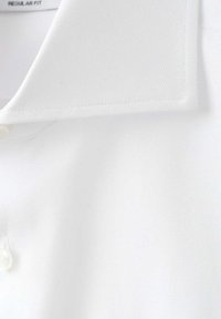 Gros plan d'un col de chemise blanche avec une texture subtile en chevrons et un bouton nacré sur une chemise coupe droite.