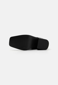 Semelle de chaussure noire présentant un design plat, une surface en caoutchouc texturée, et une forme légèrement courbée avec un orteil arrondi.