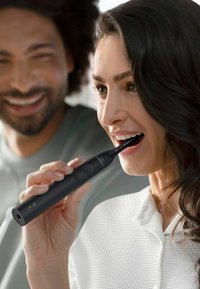 Brosse à dents électrique avec un manche noir élégant et une tête de brosse rectangulaire. Le design comprend un bouton d'alimentation et un voyant lumineux vert.