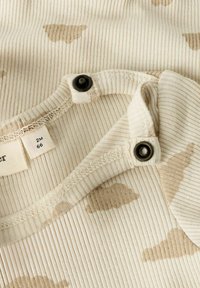 Zbliżenie beżowego, prążkowanego ubrania dla niemowląt z brązowymi chmurkami i czarnymi napami w okolicy dekoltu, metka rozmiaru pokazująca 2M 66.