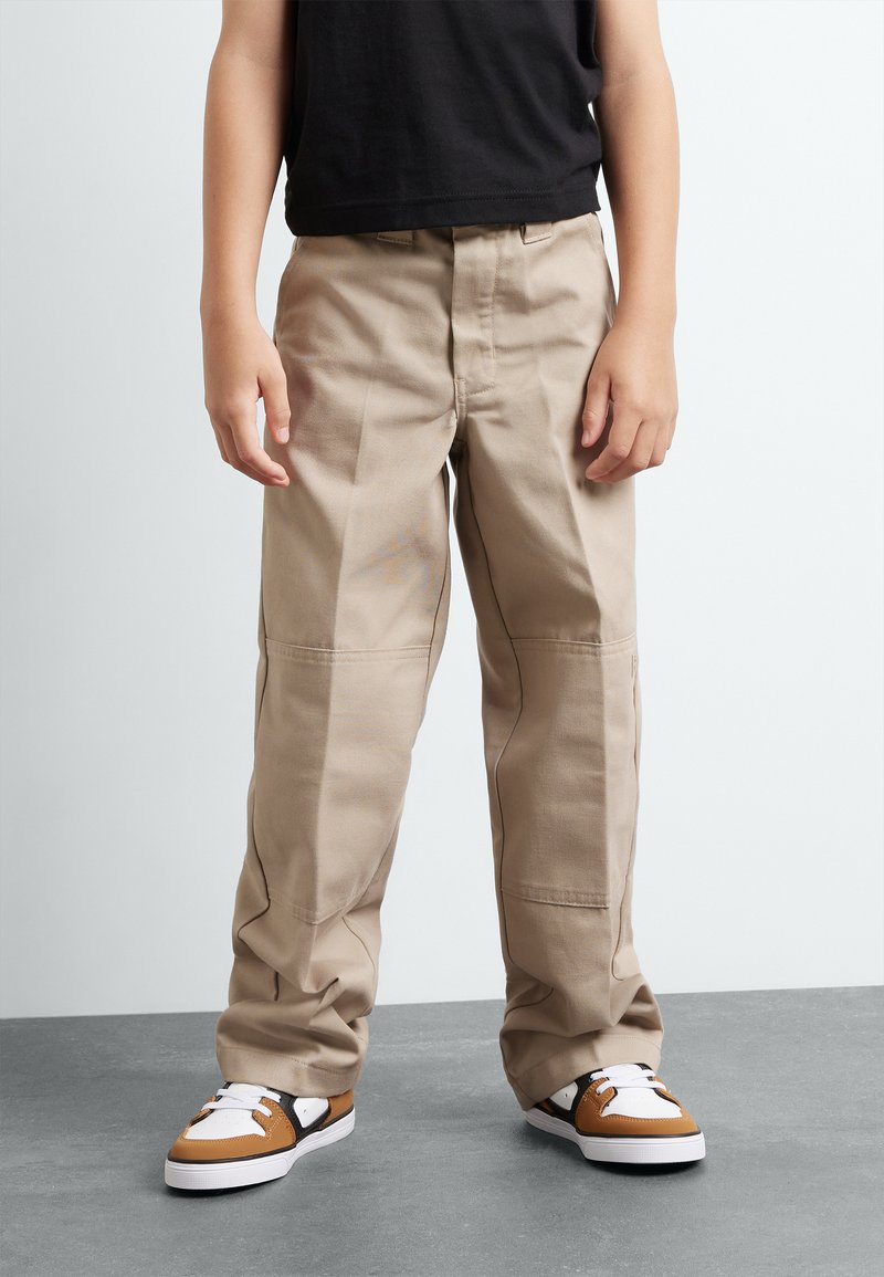 Pantalons en coton beige avec une coupe décontractée, dotés de coutures latérales, de jambes droites et de couture visible. Assortis avec des baskets marron et blanches.