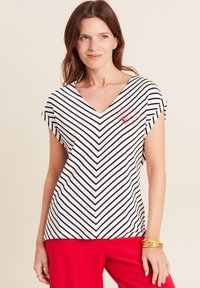 Gestreepte V-hals top in wit en marineblauw, met korte mouwen en een rood geborduurd schelpendesign op de linkerkant van de borst. Zacht materiaal.