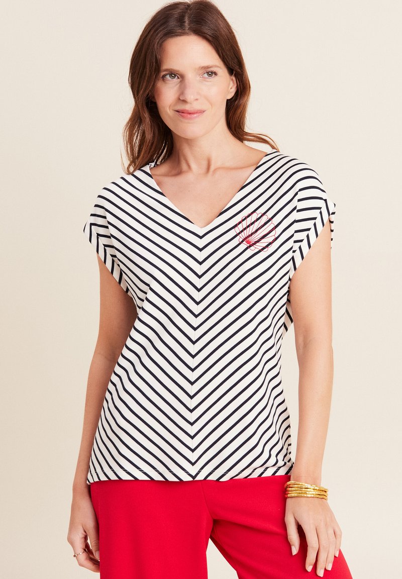 Gestreepte V-hals top in wit en marineblauw, met korte mouwen en een rood geborduurd schelpendesign op de linkerkant van de borst. Zacht materiaal.