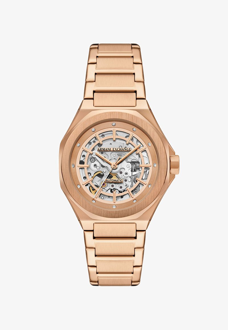 Roséguld automatisk klocka med en transparent skelettskiva, diamantdetaljer, oktagonal bezel och länkad metallarmband.