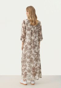 Robe longue et légère à motifs floraux avec des feuilles marron. Le vêtement a des manches trois-quarts et une coupe ample, associé à des baskets blanches.