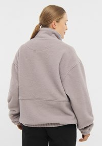 Pullover in pile di colore grigio chiaro con colletto alto, vestibilità oversize, maniche scese e tessuto testurizzato. Nessuna ferramenta o dettagli visibili.