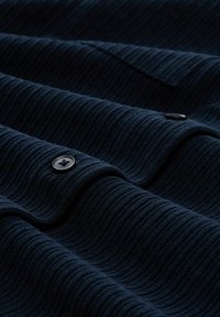 Granatowa, teksturowana tkanina z pionowymi prążkami, ozdobiona czarnym guzikiem. Miękka tekstura z subtelnymi falami i fałdami widocznymi na powierzchni.