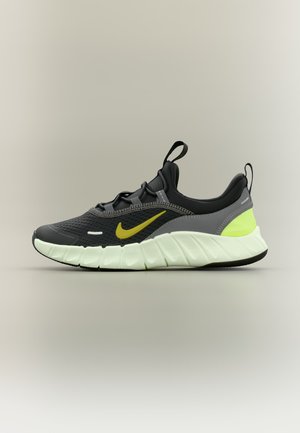 Fekete és szürke sportcipő neon sárga Nike logóval és részletekkel, fehér texturált talppal, és húzófülekkel a nyelvnél és a saroknál.