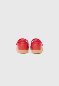 Red leather sneakers with a smooth finish, textured heel, and a gum rubber sole. Features two small loops at the heel for easy wear.
