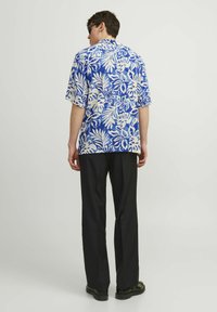 Camisa de manga corta azul y blanca con estampado floral, hecha de una tela ligera, combinada con pantalones negros. Presenta un corte relajado y un cuello abierto.