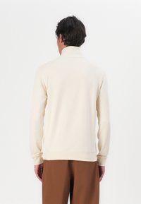 Light beige sweatshirt with a high collar, long sleeves, and ribbed cuffs. Smooth texture, relaxed fit, and plain design with no visible logos.