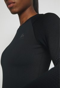 Black athletic top with long sleeves featuring a textured pattern on the shoulders. The fabric appears smooth with a fitted design.