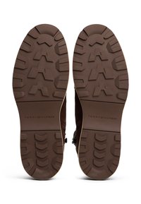 Stivali in suede marrone con suola in gomma texturizzata. La suola presenta un motivo di battistrada multidirezionale. Logo visibile sulla suola.