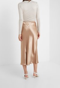 Spódnica o długości średniej, przypominająca jedwab, w jasnym odcieniu beżu, o gładkiej fakturze, rozkloszowanym kroju i z paskiem w talii. Uzupełniona o neutralne szpilki.