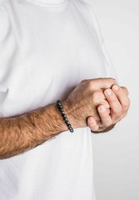 Brățară din mărgele negre, realizată din pietre lustruite, cu formă rotundă, purtată pe un încheietură cu nuanță deschisă a pielii și îmbrăcăminte de culoare deschisă.