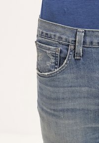 Blå denimjeans med en blekt tvätt, med en framficka, synliga sömmar och silverfärgade detaljer. Midjebandet är utan dekoration.