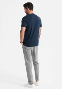 T-shirt navy a maniche corte con scollo rotondo, indossato con pantaloni grigi chiari su misura, caratterizzati da una vestibilità slim e orli arrotolati, abbinato a scarpe bianche.