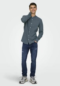 Camisa de botones azul oscuro con mangas largas, de diseño ajustado. Combinada con jeans oscuros desgastados y zapatillas grises con acentos negros.