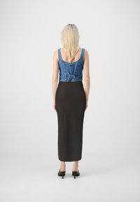Denim crop top med breda axelband och bakbälte, kombinerat med en figurnära, golvlång svart kjol. Modellen bär svarta klackar.