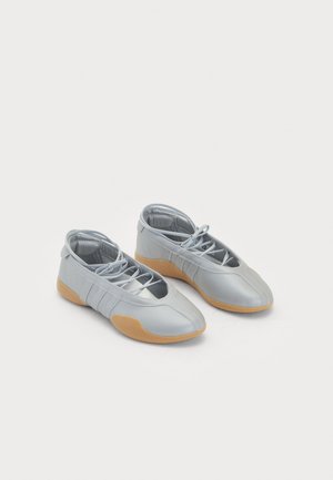 Sapatos sintéticos prateados com perfil baixo, sola de borracha e fecho de atacadores. Apresenta três linhas de destaque nas laterais e textura suave.