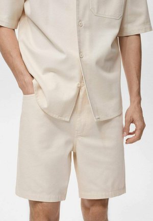 Beige Kurzarm-Hemd mit Knopfleiste und Tasche sowie passenden beigen Shorts. Baumwollstoff, lässige Passform, glatte Textur, minimales Design.