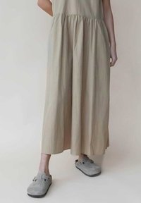 Robe beige clair avec taille froncée, jupe fluide ; associée à des sabots gris avec une sangle et une surface texturée. Design minimaliste.